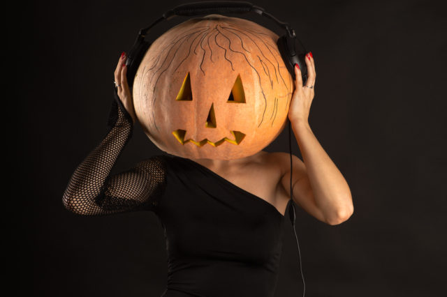 woman with a pumpkin on head with headphones listening music